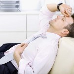 Mid-adult businessman lying on sofa at office, looking tired, eyes closed. Bright background.